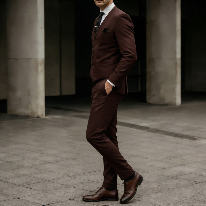 Side portrait of a man wearing a fitted burgundy suit in a formal style
